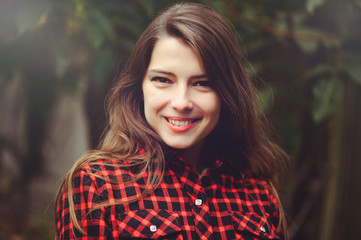 Smiling young brunette woman posing in the courtyard of her residence in a red checkered shirt is happy, portrait of happy carefree, health