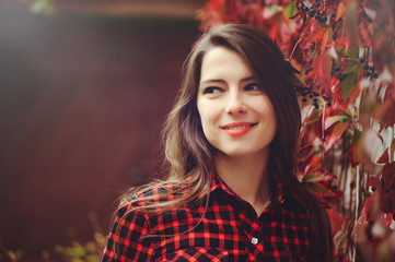 Smiling young brunette woman posing in the courtyard of her residence in a red checkered shirt is happy, portrait happy carefree, health in cushy tones