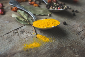 Close up view of a vintage spoon filled with curcuma or turmeric, with allspice pepper and spilled...