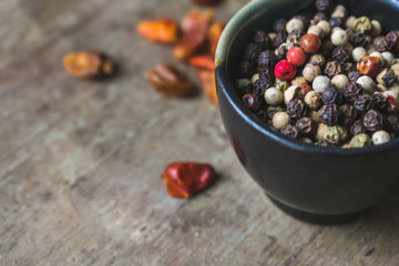 Close up view of allspice, white, green, black and red pepper, on old rustic background with dried chilly peppers. Vintage toned. Spices background