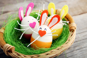 Eggs with funny rabbit faces in basket on grey wooden table