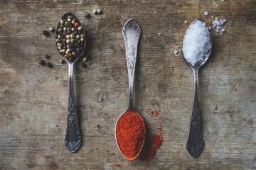 Top view of colorful spices in vintage spoons and dried chilly and bay leaves on old rustic background. Vintage toned. Spices background