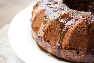 Homemade chocolate cake with chocolate syrup topping on white plate. Ring cake. Over wooden table.