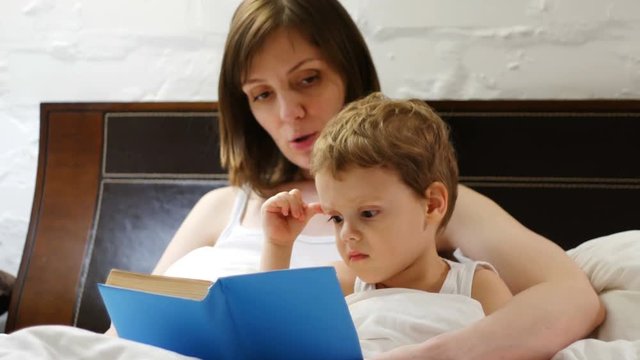 Mother and her three years old baby boy are reading book in bed
