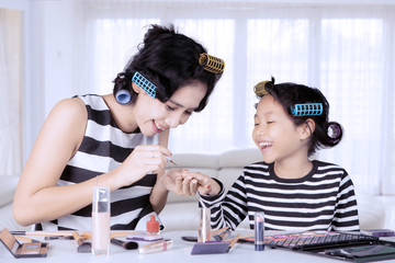 Young asian mother and daughter with hair curlers are doing nail polish at home