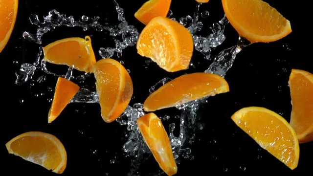 Slices of orange with water bouncing against to the camera on a black background in slow motion