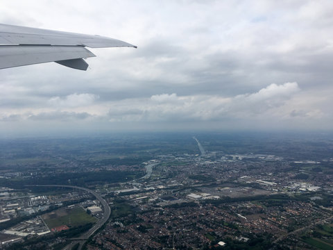 Looking out of an airplane window, rolling white clouds stretch out in the distance, blue sky on a sunny summer day. View of clouds and airplane wing from flight over Brussels, Belgium, Europe.