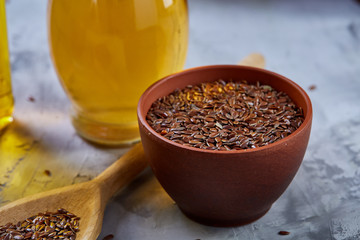 Flax seeds in bowl and flaxseed oil in glass bottle on light textured background, top view, close-up, selective focus