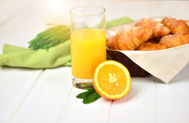 Morning breakfast with a fresh juice and croissants on a white wooden table.