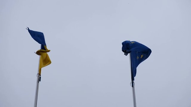 Flag of Ukraine and flag of European Union fluttering on a background of a rainy sky
