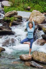 Woman in yoga asana Vrikshasana tree pose at waterfall outdoors