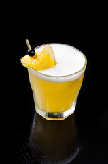 Yellow drink with lime, ginger, honey and ice. Organic strong cocktail in a glass with decoration root and berry, on black background. Bar alcohol menu, season.