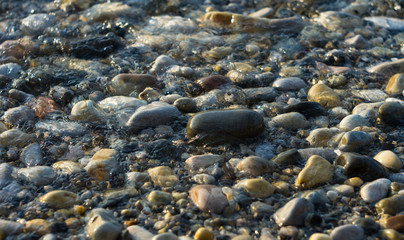 pebble stones on the sea beach, the rolling waves of the sea with foam