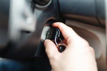 The driver of the man gets a car with a key. The hand inserts the key into the ignition and starts the car. Hand put the car key to the keyhole starting the car.
