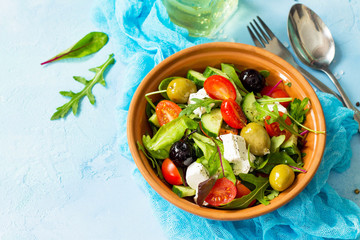 Greek salad with fresh vegetables, feta cheese and black olives on a blue stone or concrete table.