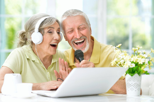 happy senior couple singing karaoke with laptop
