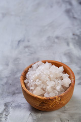 Large white sea salt in a natural wooden bowl on white background, top view, close-up, selective focus