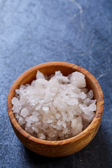 Large white sea salt in a natural wooden bowl on white background, top view, close-up, selective focus