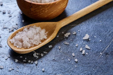 Crystal sea salt in a wooden spoon on dark background, top view, close-up, selective focus.
