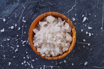 Large white sea salt in a natural wooden bowl on white background, top view, close-up, selective focus