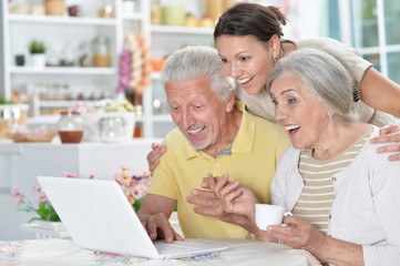 happy senior couple with adult daughter using laptop 