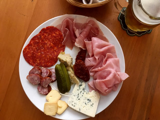 Top view of a charcuterie plate and glass of beer on a wooden table. Appetizer plate of cheese, cured meats, and pickles. Looking down on meet and cheese plate and local pub in Prague.