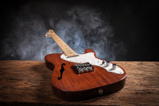 Vintage electric guitar on a wood raw table. Musical instrument. Black background with smoke