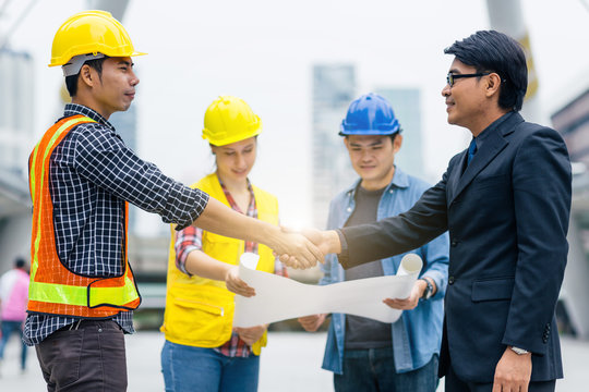 Handshake between engineer and manager, team meeting outdoor using blueprint