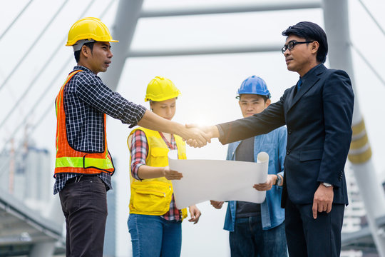 Handshake between engineer and manager, team meeting outdoor using blueprint