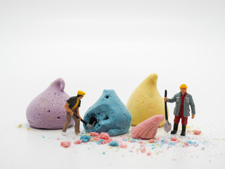 Miniature worker and colorful merengue on white background, selective focus. sweet dessert