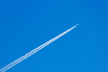 Modern jet plane with white condensation track flies on a blue sky background