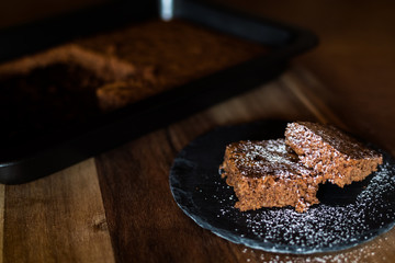 Saftiger Kuchen aus Zartbitterschokolade mit Mandeln vom Blech angerichtet auf einer Schieferplatte dekoriert mit Puderzucker