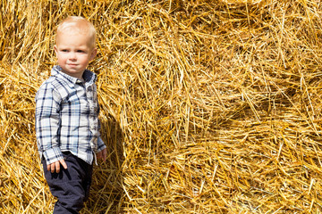 little fashionable boy in the background of a haystack