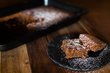 Saftiger Kuchen aus Zartbitterschokolade mit Mandeln vom Blech angerichtet auf einer Schieferplatte dekoriert mit Puderzucker