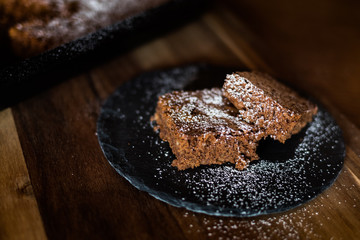 Saftiger Kuchen aus Zartbitterschokolade mit Mandeln vom Blech angerichtet auf einer Schieferplatte dekoriert mit Puderzucker