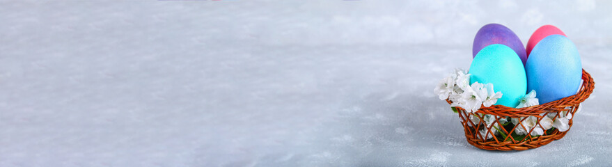 Colored Easter eggs in a basket on a gray concrete background. Banner