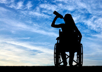 Silhouette of a disabled woman in a wheelchair drinking water from a plastic bottle