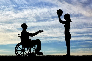 Obraz na płótnie Canvas Silhouette of a disabled man in a wheelchair and his wife playing ball together