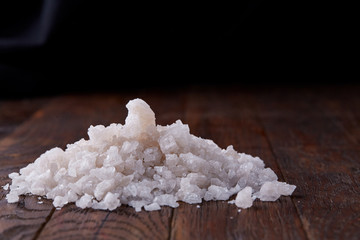 Pile of salt crystals on the dark wooden background, top view, flat lay, shallow depth of field