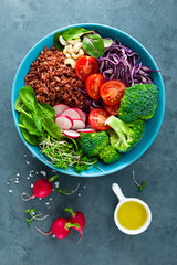 Buddha bowl meal with kale, spinach and chard leaves, brown rice, tomato, broccoli, radish, fresh green sprouts and pine nuts. Healthy balanced nutrition. Vegetarian food. Overhead view