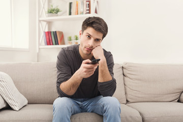 Young boring man watching television at home