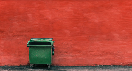 green garbage container on a red wall background