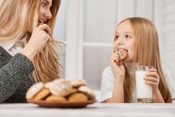 Photo of mother and daughter eating cookies and drinking milk. Both girls have blonde straight...