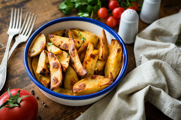 Potato wedges or baked potato garnished with parsley on old rustic table. Selective focus