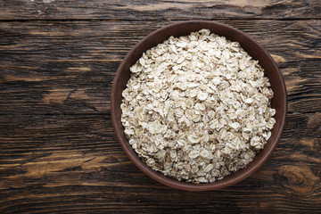 raw oatmeal in a bowl, on a brown wooden table.
