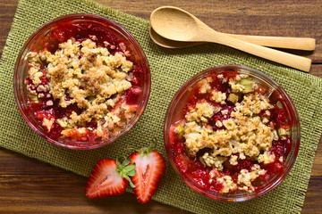 Baked strawberry and rhubarb crumble in glass bowls, photographed overhead on wood with natural...