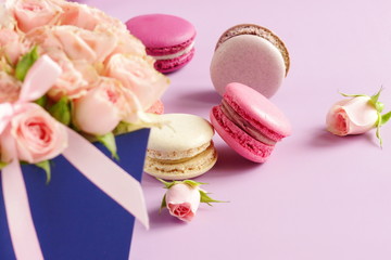 Beautiful holiday background. macaroons in pastel colors with bouquet of pink roses flowers on a pale purple  background.Holiday background.copy