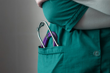 doctor in green uniform stands with arms crossed stethoscope lies in pocket