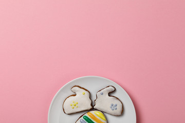 Homemade cookies in the form of Easter figurines in a plate on a pink background with space for text, top view