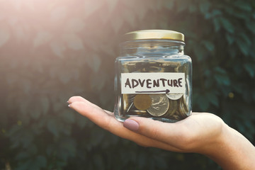 Hand holding glass jar with coins for adventure